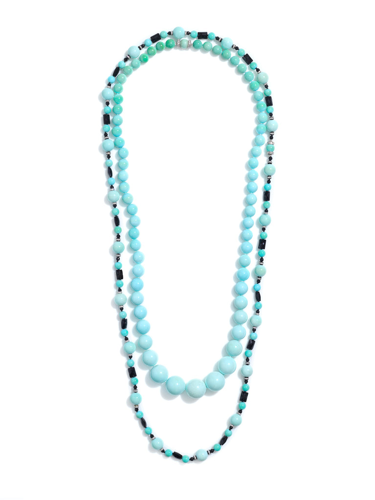 Two beaded necklaces. One a graduated strand of light blue to greenish-blue Persian turquoise bands with two small platinum diamond rondels at the clasp. The other strand alternating two sizes of round turquoise beads with black onyx rectangular beads and platinum and diamond rondels in  a repeating pattern. Photographed on a white background. 